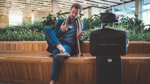 Amex-Punkte in Meilen umwandeln - Mann sitzt mit Koffer und Kreditkarte in der Hand am Flughafen.