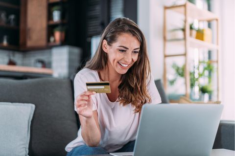 Amex Offers: Frau sitzt mit Kreditkarte in der Hand auf einem Sofa vor dem aufgeklappten Laptop.