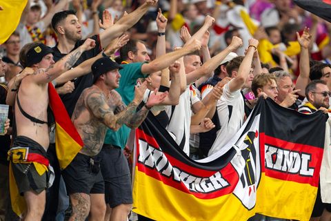 Deutsche Fußballfans halten im Stadion grölend ihre Flaggen hoch