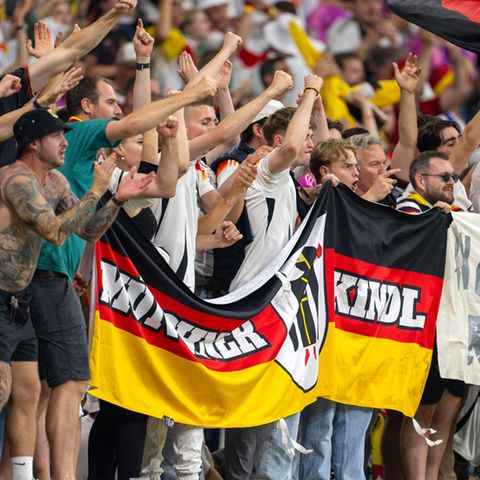 Deutsche Fußballfans halten im Stadion grölend ihre Flaggen hoch
