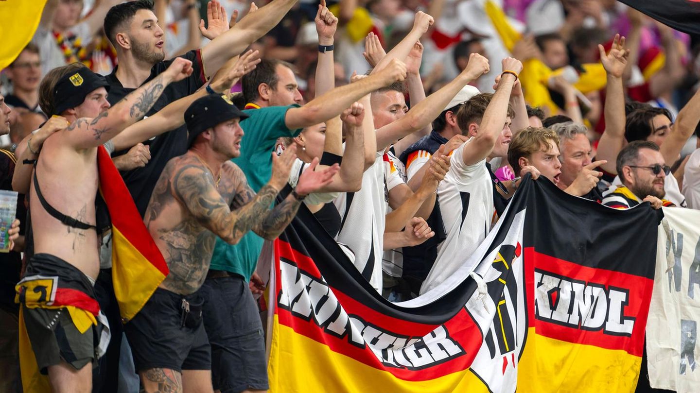 Deutsche Fußballfans halten im Stadion grölend ihre Flaggen hoch