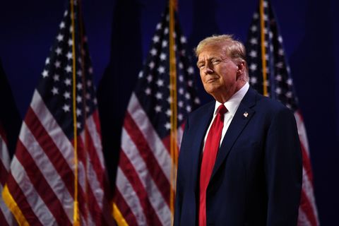 Donald Trump steht vor amerikanischen Flaggen und sieht triumphierend aus