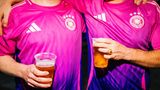 Zwei Männer im pinken DFB-Trikot mit Bierbechern in der Hand