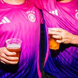 Zwei Männer im pinken DFB-Trikot mit Bierbechern in der Hand