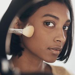 Make-up Pinsel reinigen: Eine Frau hält sich einen Pinsel an die Wange.