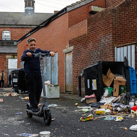 Ein Junge fährt mit einem Roller durch eine heruntergekommene Seitenstraße. In den ärmsten Gegenden Großbritanniens ist die abwesende Müllabfuhr für viele die kleinste Sorge