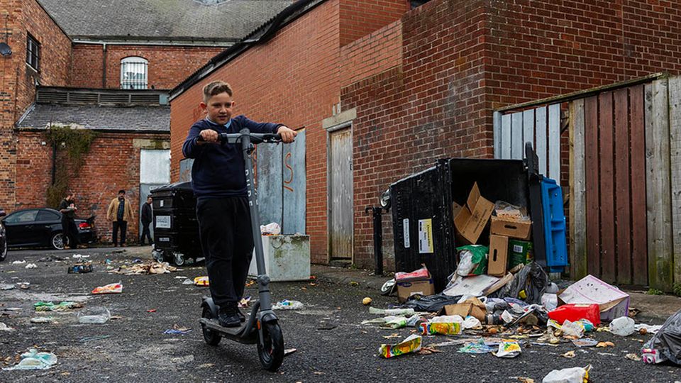 Ein Junge fährt mit einem Roller durch eine heruntergekommene Seitenstraße. In den ärmsten Gegenden Großbritanniens ist die abwesende Müllabfuhr für viele die kleinste Sorge
