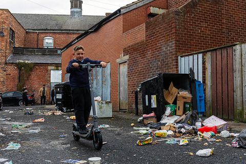 Ein Junge fährt mit einem Roller durch eine heruntergekommene Seitenstraße. In den ärmsten Gegenden Großbritanniens ist die abwesende Müllabfuhr für viele die kleinste Sorge