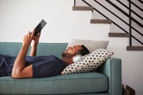 Mann liegt mit Kopfhörern und Tablet entspannt auf der Couch und schaut eine Serie