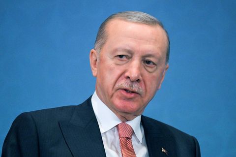 Recep Tayyip Erdogan sitzt in Anzug und Krawatte vor einem himmelblauen Hintergrund