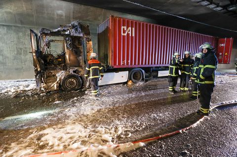 Feuerwehrleute stehen neben einem ausgebrannten Lkw im Elbtunnel in Hamburg