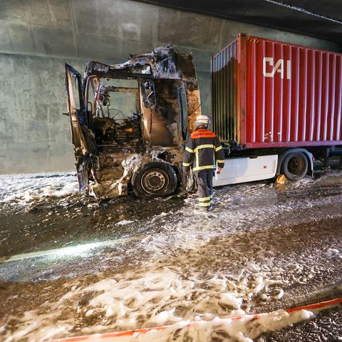 Feuerwehrleute stehen neben einem ausgebrannten Lkw im Elbtunnel in Hamburg
