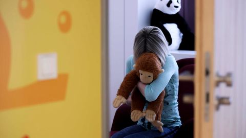 Eine junge Frau sitzt mit einem Kuscheltier im Arm, Symbolfoto Kindesmissbrauch