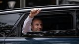 Präsident Emmanuel Macron hebt den Daumen aus seinem Auto