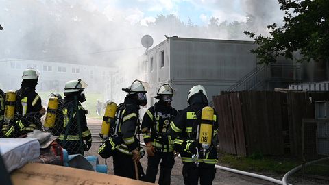 In Buchholz stehen Feuerwehrleute vor brennenden und rauchenenden Wohncontainern