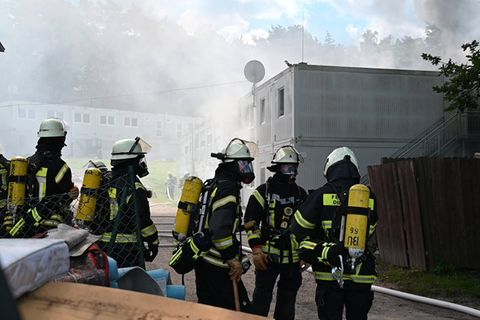 In Buchholz stehen Feuerwehrleute vor brennenden und rauchenenden Wohncontainern