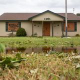 "Go away Beryl" steht auf der Holzplatte, die das Fenster links sichert. Die durchgestrichenen Namen vorheriger Stürme zeigen: Das Haus hat schon einiges überstanden