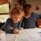 Die beiden Jungs blicken am Tisch im Airstream auf eine Karte von Norwegen