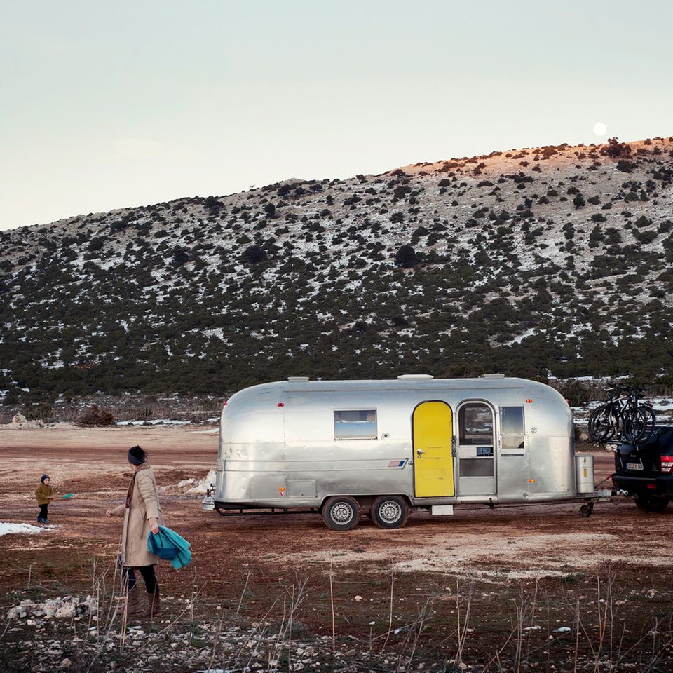Vor dem geparkten Airstream spielen die beiden Jungs in den letzten Schneeresten. Im Hintergrund karge Berge.
