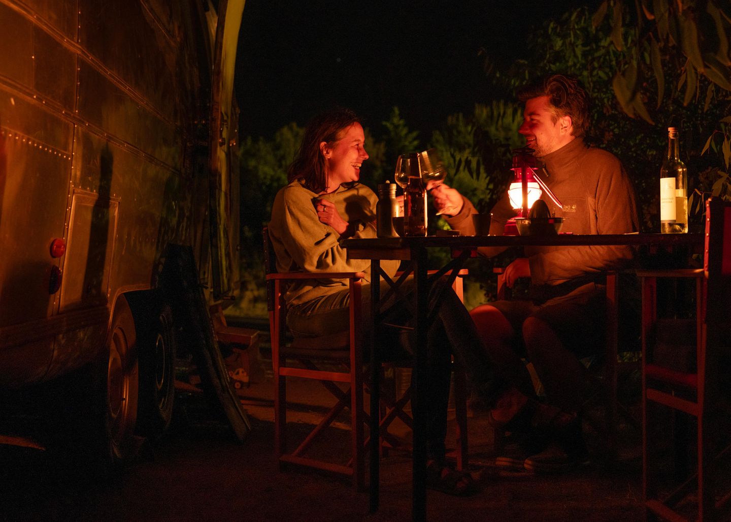 Die Eltern sitzen abends bei einem Glas vor dem Airstream zusammen und unterhalten sich im Schein einer Laterne