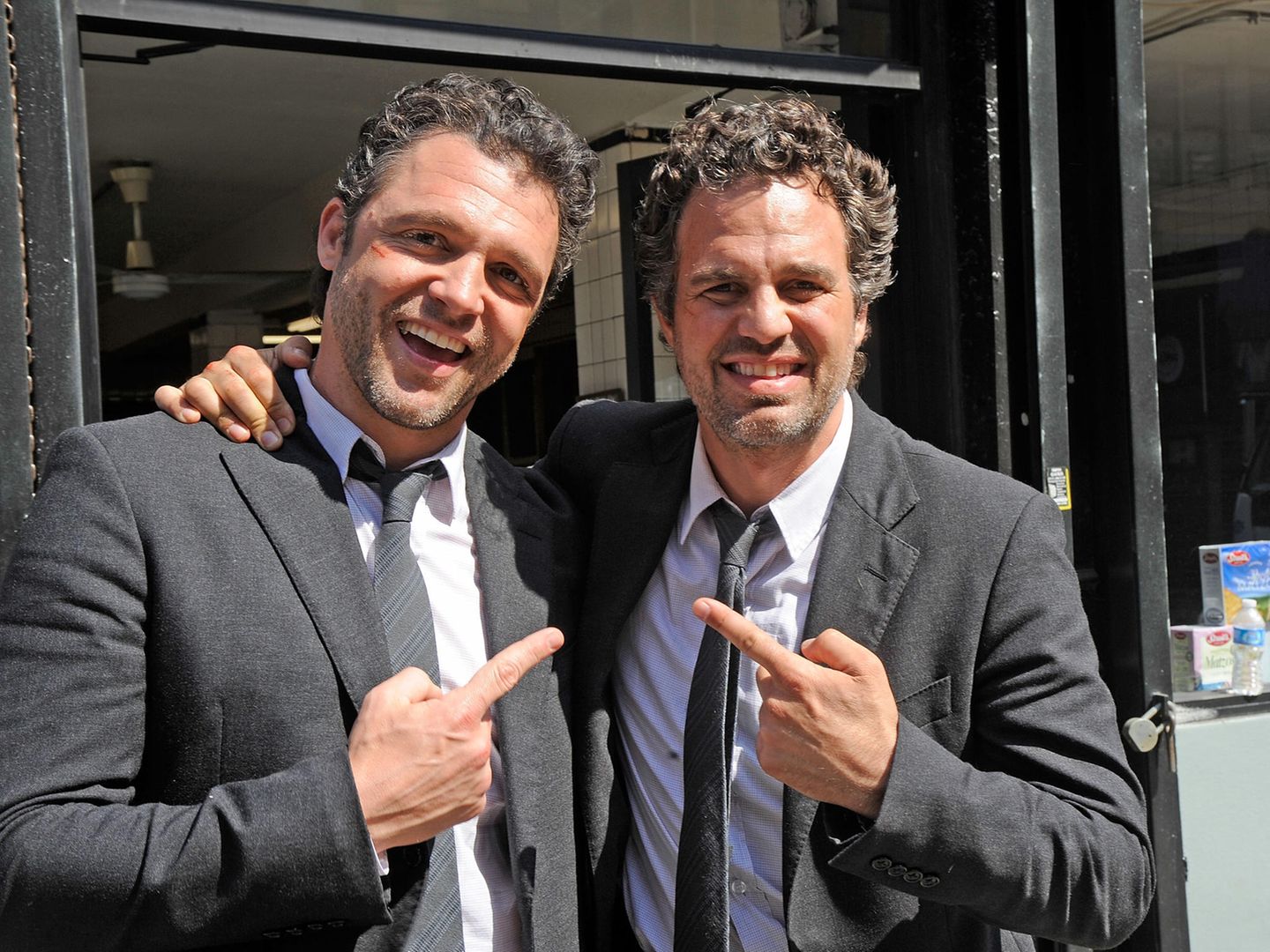 Anthony Molinari und  Mark Ruffalo, in gleichem Kostüm, schauen in die Kamera und zeigen gegenseitig aufeinander.