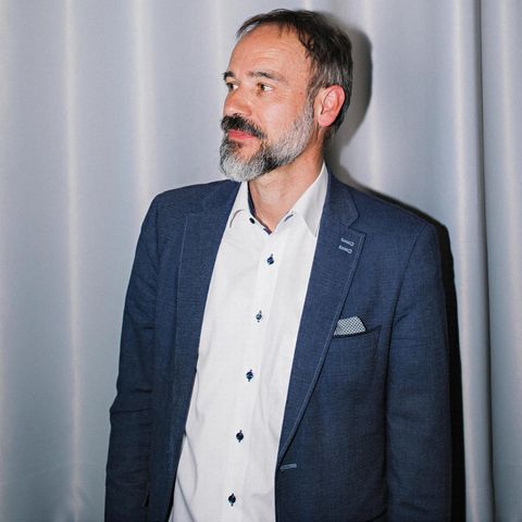 Porträt von Stefan Pohlmann vor einem hellblauen Vorhang
