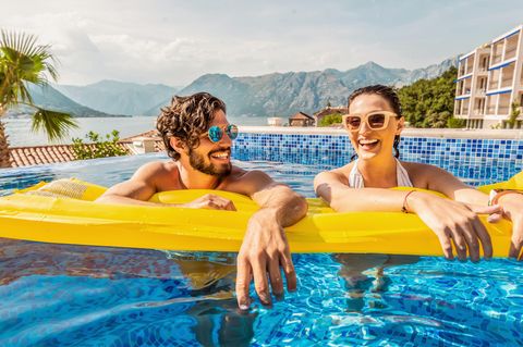Pauschalurlaub: Paar treibt auf einer Luftmatratze im Pool am Urlaubsort