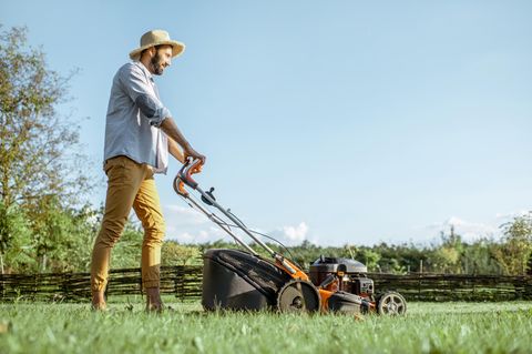 Rasenmähen bei Sommerhitze: Mann mit Sonnenhut mäht den Rasen.