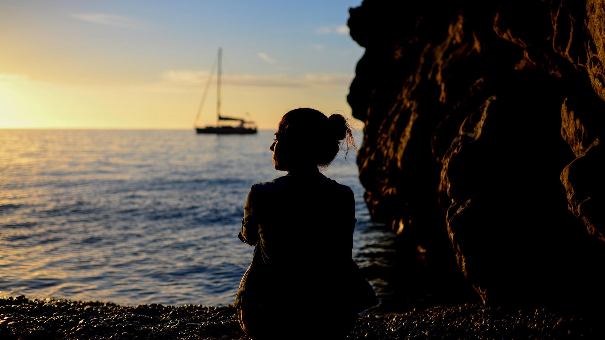 Symbolbild Depressionen: Nachdenkliche Frau sitzt im Sonnenuntergang am Meer