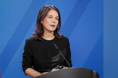 Annalena Baerbock spricht vor einer blauen Wand in ein Mikrofon