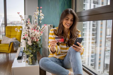 Cashback-Kreditkarten: Frau mit Handy und Kreditkarte in der Hand.