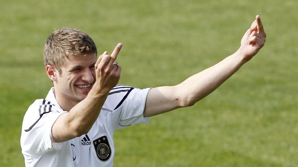 Thomas Müller zeigt auf dem Trainingsplatz im DFB-Dress lächelnd jemandem beide Mittelfinger