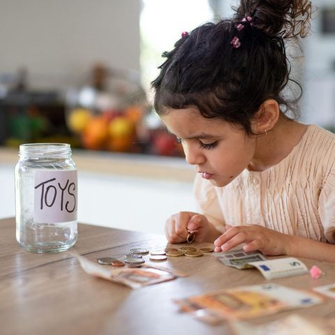 Taschengeld: Mädchen zählt ihr Geld. Daneben ist eine Spardose mit der Beschriftung "Toys"