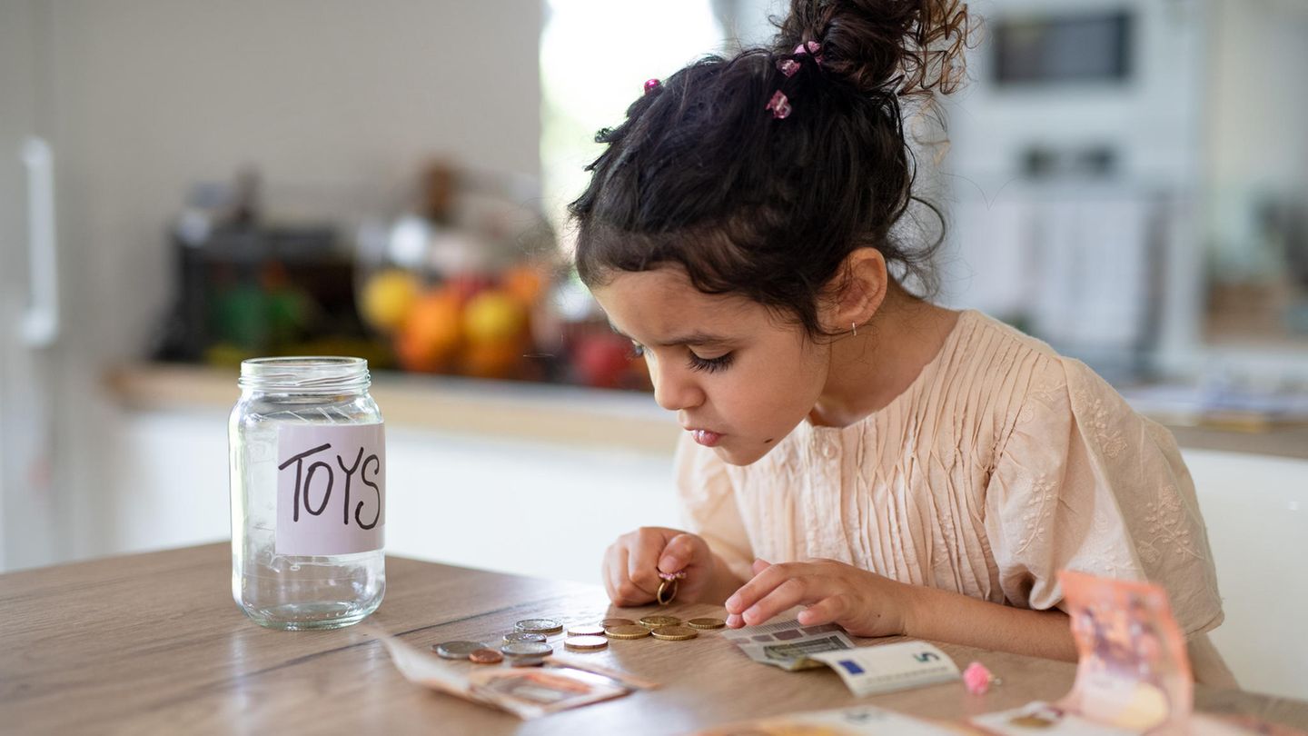 Taschengeld: Wie Kinder den richtigen Umgang mit Geld lernen Taschengeld: Mädchen zählt ihr Geld. Daneben ist eine Spardose mit der Beschriftung "Toys"