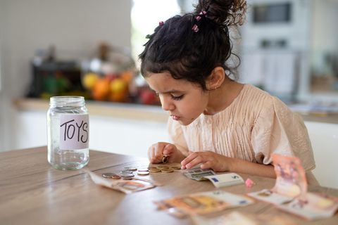 Taschengeld: Mädchen zählt ihr Geld. Daneben ist eine Spardose mit der Beschriftung "Toys"