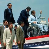 Wallace wird in einem Rollstuhl auf ein Rednerpult geschoben