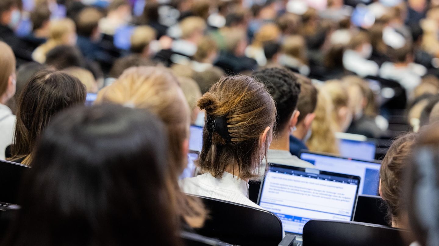 Juniorstudium Eine Studentin sitzt im Hörsaal zwischen anderen Studenten und schaut in ihr Laptop.