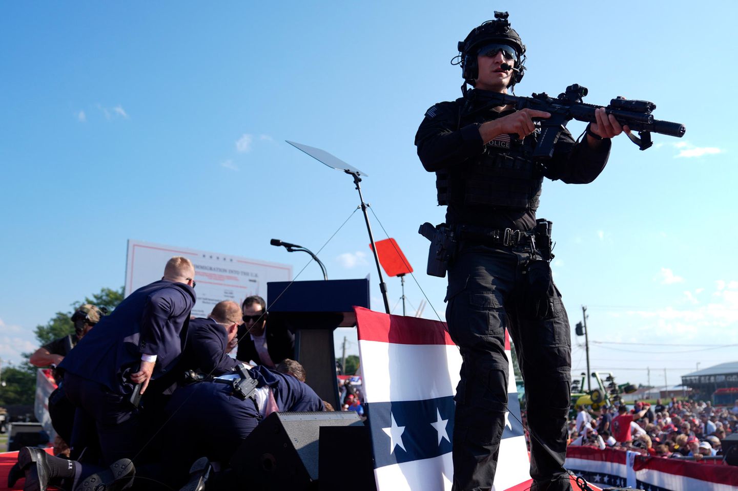 Trump-Attentat: Sekunden nach dem Attentat auf Donald Trump wird er von Mitarbeitern des Secret Service abgeschirmt. Ein schwer bewaffneter Polizist sichert die Lage. Sekunden nach dem Attentat auf Donald Trump wird er von Mitarbeitern des Secret Service abgeschirmt. Ein schwer bewaffneter Polizist sichert die Lage.