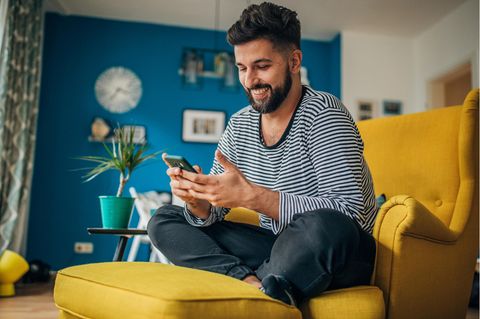 Happy SIM: Mann sitzt glücklich mit einem Handy auf einem Sessel.