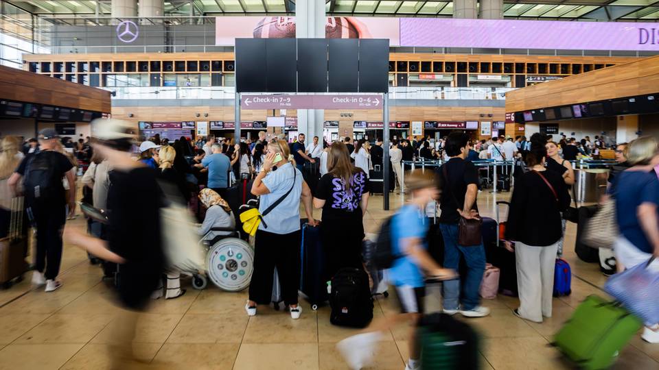 Zahlreiche Fluggäste warten am Hauptstadtflughafen BER vor einer schwarzen Anzeigetafel