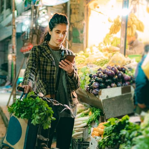 Eine Frau schaut auf einem Markt mit ernstem Blick auf ihr Handy