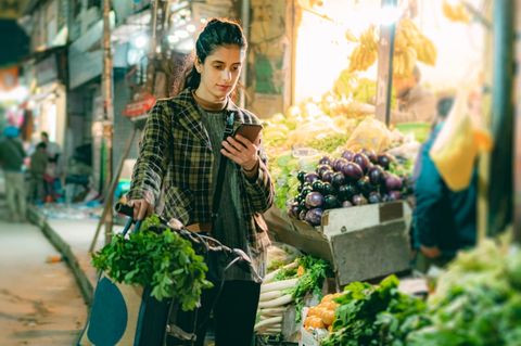 Eine Frau schaut auf einem Markt mit ernstem Blick auf ihr Handy