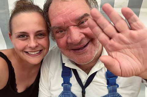 Eine Frau und ein Mann nebeneinander. Er winkt in die Kamera