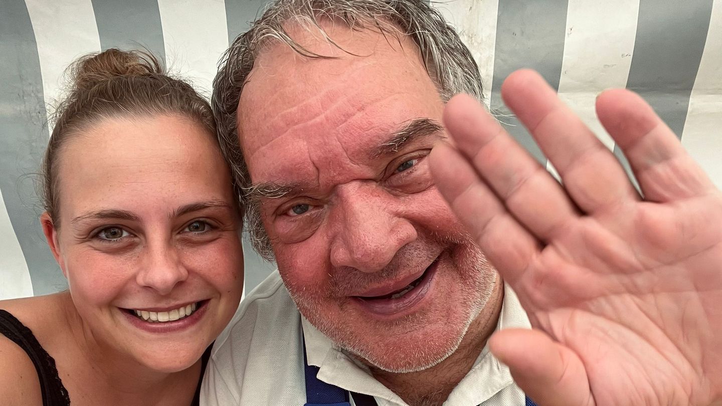 Eine Frau und ein Mann nebeneinander. Er winkt in die Kamera