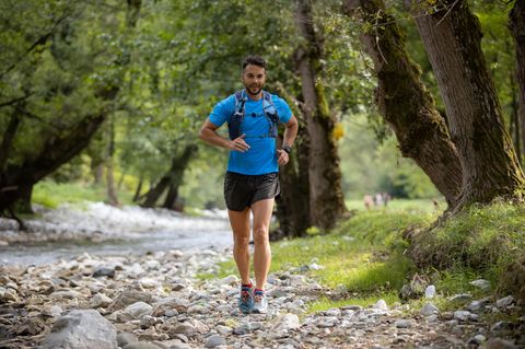 Trendsport Trailrunning: Mann läuft mit Trinkweste neben einem Flussbett
