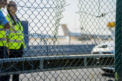 Mitarbeiter stehen an dem zerstörten Zaunabschnitt, durch den die Klima-Aktivisten auf das Flughafengelände eingedrungen sind