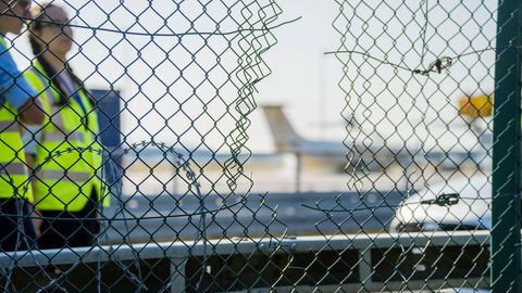 Mitarbeiter stehen an dem zerstörten Zaunabschnitt, durch den die Klima-Aktivisten auf das Flughafengelände eingedrungen sind