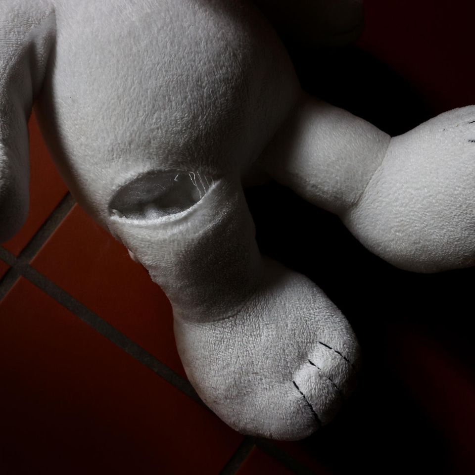 Ein Teddybär mit einem Riss im Bein auf roten Fliesen