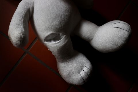 Ein Teddybär mit einem Riss im Bein auf roten Fliesen