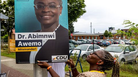 Abimnwi Awemo hängt ein Wahlplakat von sich in Cottbus auf
